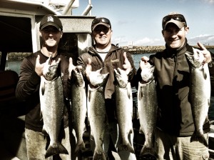 Three men standing on a boat holding large fish they have caught, smiling at the camera.